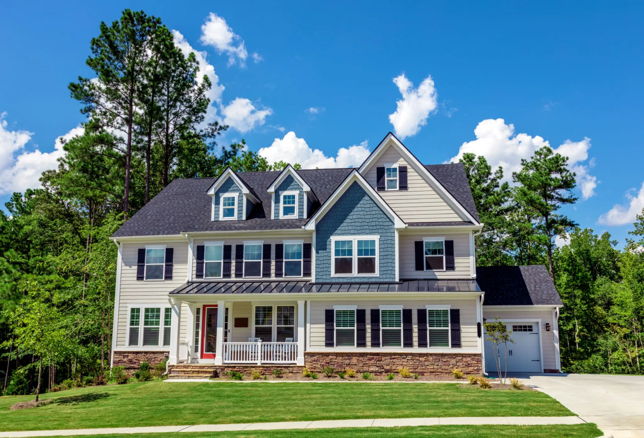 Large suburban house with a well-kept lawn under a blue sky.